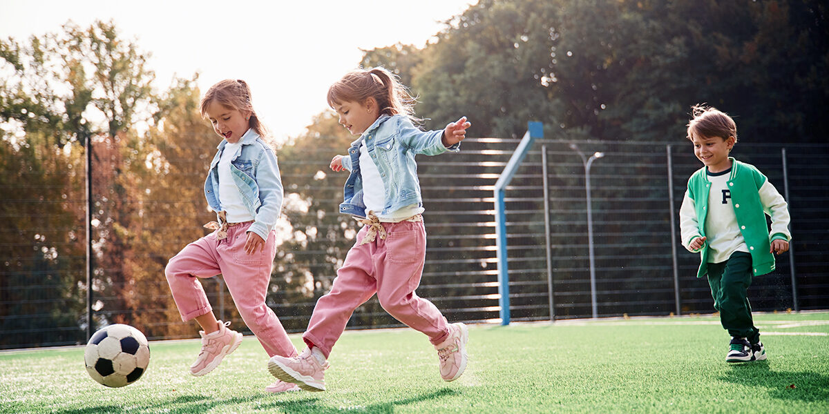 Running with ball. Kids are having fun on the green soccer field together.